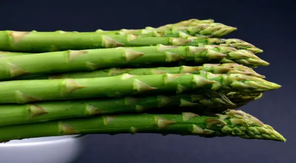 A stack of fresh green asparagus spears with water droplets, against a dark background.