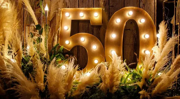 Złote litery "50" z żarówkami, otoczone puszystymi trawami i zielenią, tworzą magiczną dekorację na 50 urodziny.