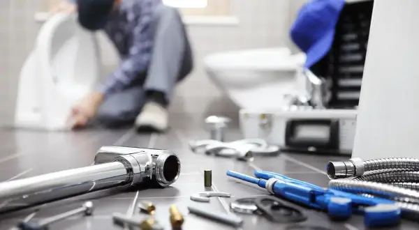 Idraulico al lavoro su un water, con attrezzi e tubi in primo piano. La pendenza scarico cucina è fondamentale per un corretto deflusso.
