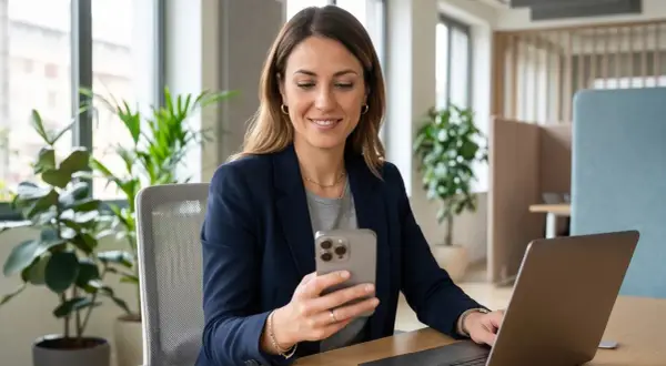 Donna sorridente al telefono, con un laptop aperto. Sembra che stia organizzando la sua astensione dal lavoro.