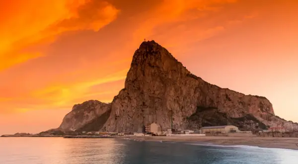 Gibraltar, czy to państwo, majestatycznie wznosi się nad morzem o zachodzie słońca. Pomarańczowe niebo maluje dramatyczne tło dla skalistej skały.