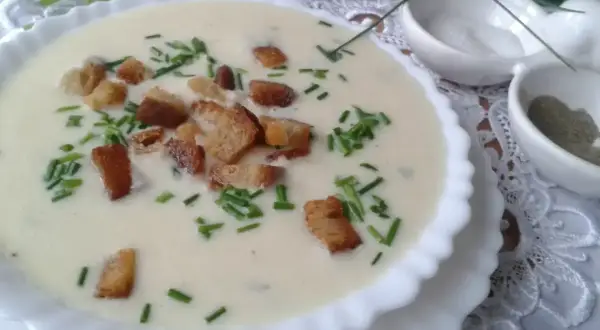 Kremowa zupa porowa z grzankami i szczypiorkiem w białej misce.