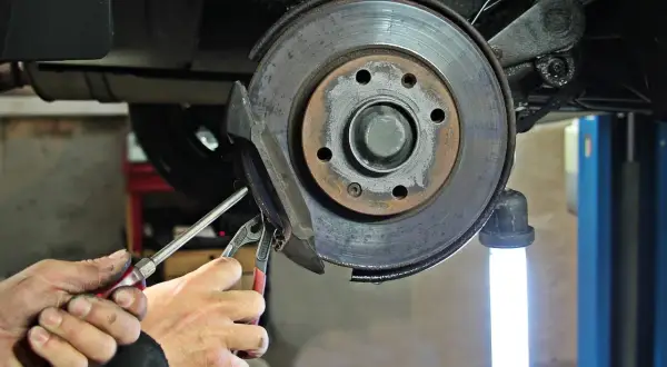 Mains d'un mécanicien utilisant des outils pour changer un disque de frein usé sur une voiture.