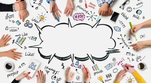 Ludzie tworzą burze mózgów, rysując na białej powierzchni słowa: "teamwork", "idea", "vision", "plan", "strategy", "growth", "team", "think", "talk", "network", "share", "project", "success".
