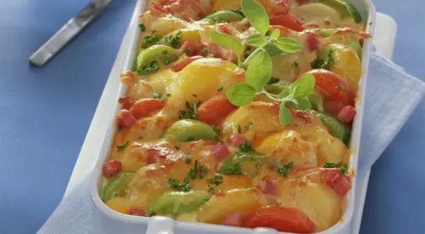 Herzhaftes Kartoffel Lauch Gratin mit Tomaten und Speck, überbacken mit goldbraunem Käse und garniert mit frischen Kräutern.
