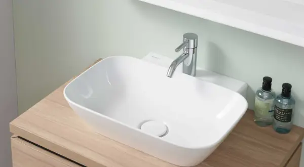 Nowoczesna, mała umywalka do WC na drewnianym blacie, z chromowaną baterią i dwoma buteleczkami płynu do rąk.