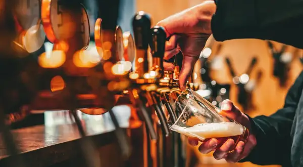 Mano che versa birra da una spillatrice, creando una schiuma perfetta. La spillatura alla tedesca è un'arte.