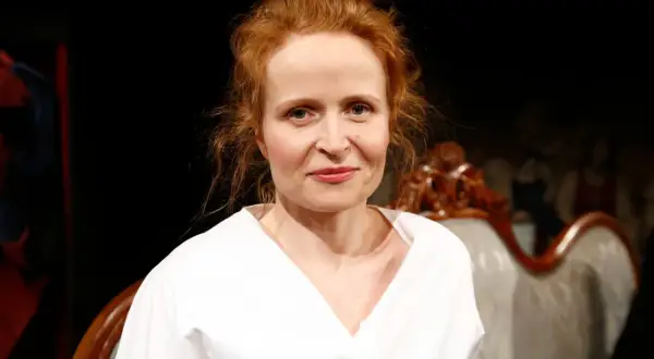 Dominika Kluźniak w białej koszuli, aktorka znana z filmów, seriali i programów, uśmiecha się lekko.