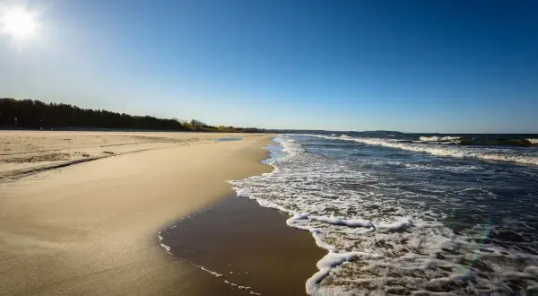 Słoneczny dzień nad polskim morzem. Piaszczysta plaża, szum fal i błękitne niebo tworzą idealny krajobraz.
