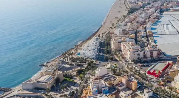 Vista aérea de la costa de Almería, Roquetas de Mar, con el mar azul, la playa, edificios residenciales y un castillo histórico.