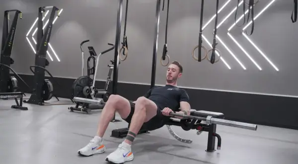 Man utför hip thrusters med skivstång på en bänk i ett modernt gym.