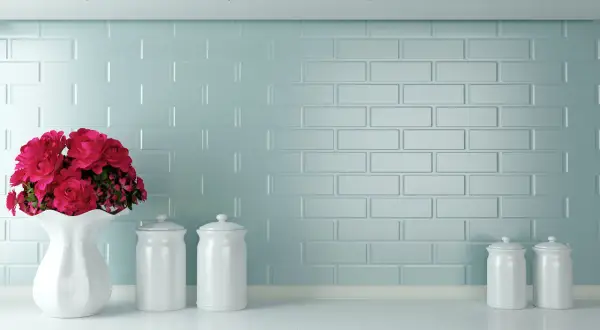 Un vaso bianco con fiori rossi e barattoli su un piano di lavoro. Un'idea per come verniciare le piastrelle della cucina con un tocco di colore.