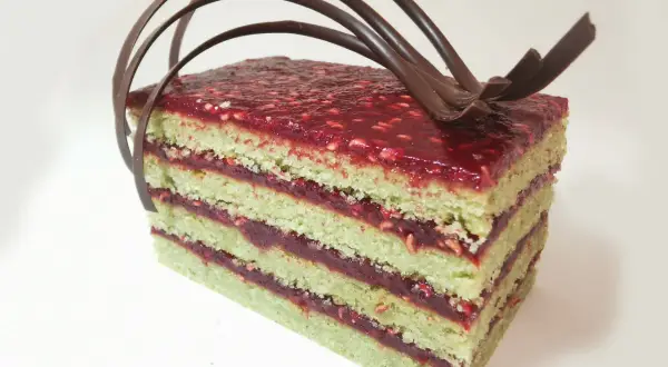 Gâteau pistache framboise mascarpone, une tranche aux couches vertes et rouges, garnie de chocolat.