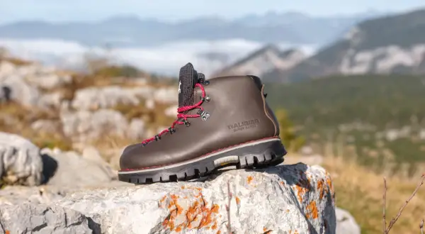 Une bonne chaussure de marche marron, lacets rouges, sur un rocher, avec des montagnes brumeuses en arrière-plan.