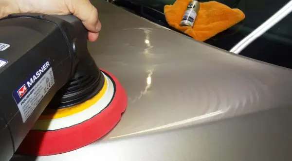 Nakładanie powłoki ceramicznej na lakier samochodu za pomocą polerki. Pomarańczowa ściereczka i butelka z preparatem K2.