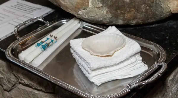 Sur un plateau argenté, des bougies ornées de colombes et d'une croix bleue, symboles de la démarche baptême, attendent près d'une coquille et de serviettes blanches.