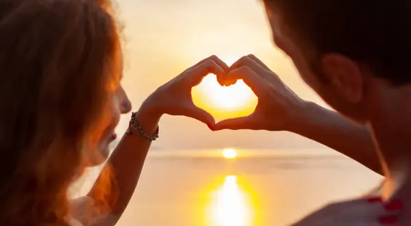 Ett par formar ett hjärta med händerna mot en solnedgång, en symbol för olika typer av relationer.