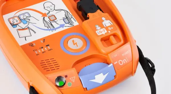 Pomarańczowy AED gotowy do użycia. Schemat pokazuje, jak prawidłowo umieścić elektrody do defibrylacji.