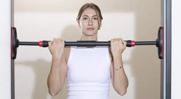 Frau hält Klimmzugstange Türrahmen Test. Einfache Montage für das Training zu Hause.