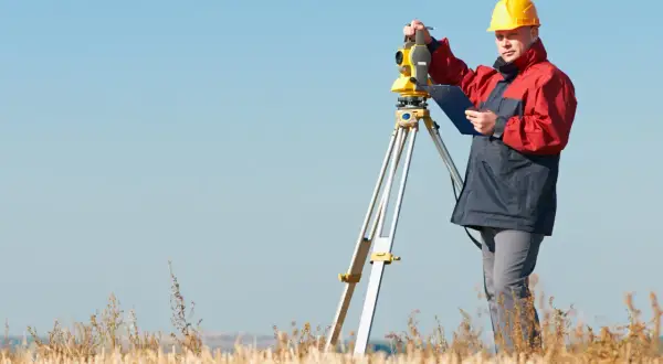Geodeta w żółtym kasku pracuje z tachimetrem w polu. Zastanawiasz się, ile kosztuje geodeta?