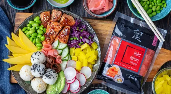 Kolorowy bowl z kawałkami łososia, edamame, mango, awokado, ryżowymi kulkami i marynowanym imbirem. Obok opakowanie różowego imbiru.