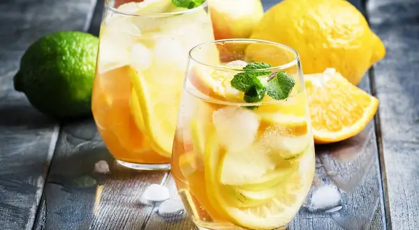 Två glas med uppfriskande vit sangria fyllda med frukt och is. Citroner, äpplen och apelsiner ger en härlig smak.