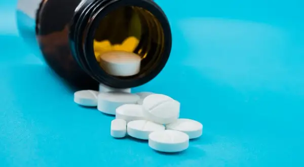 Białe tabletki, w tym jedna z nacięciem, wysypują się z brązowej butelki. To może być vicodin.