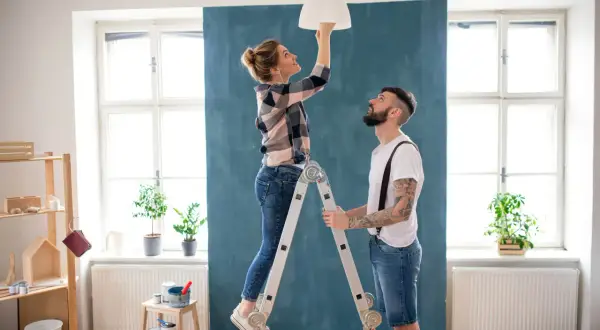 Coppia installa un lampadario, una delle migliorie che aumentano il valore di un immobile.