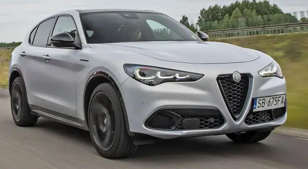 Srebrny Alfa Romeo Stelvio pędzi po drodze, jego sportowy design przyciąga wzrok.