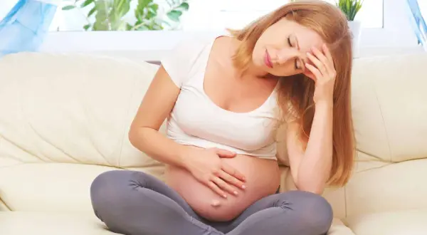 Ciężarna kobieta z bólem głowy, trzymająca się za czoło. Czuje dyskomfort w okolicy spojenia łonowego.