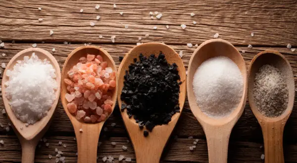 Cinco cucharas de madera muestran una composición de la sal: blanca gruesa, rosa del Himalaya, negra, fina blanca y con hierbas.