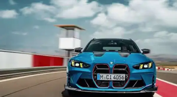 Niebieskie BMW M3 Touring pędzi po torze wyścigowym, chmury na niebie dodają dynamiki.