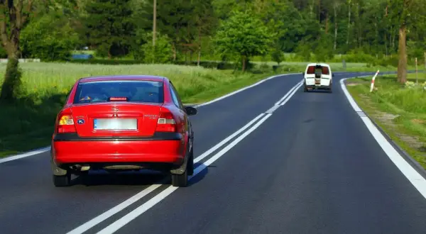 Czerwony Opel próbuje wyprzedzanie na podwójnej ciągłej, mandat murowany. Biały bus jedzie z przodu.