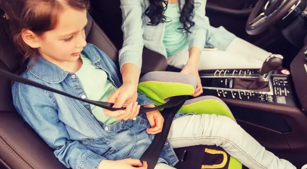 Ein Kind im Kindersitz wird angeschnallt. Die Frage "ab wann darf ein Kind vorne sitzen" ist hier relevant, da sie auf dem Beifahrersitz sitzt.