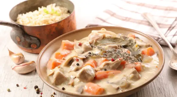 Un delicioso blanquette de ternera con zanahorias y champiñones en una cremosa salsa, servido con arroz blanco.