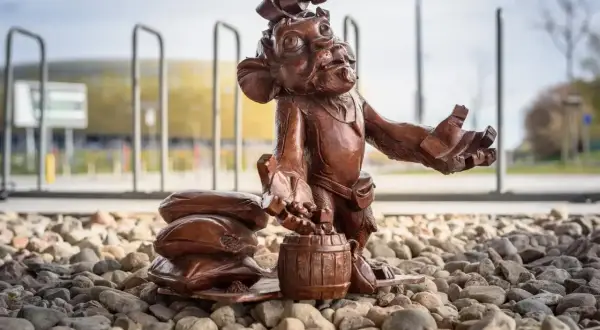 Figurka krasnala z beczką i workami, jeden z lwy gdańskie, stoi na kamieniach przed stadionem.