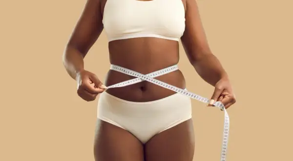 Une femme mesure sa taille avec un mètre ruban, symbolisant son objectif de perdre 5 kilos en 1 mois.