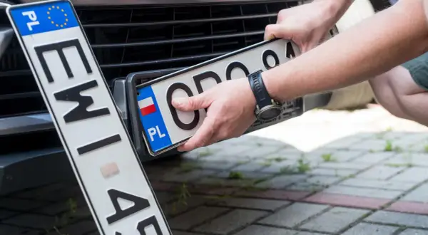 Ręce montują polską tablicę rejestracyjną. Nowe oznaczenie pojazdu gotowe do drogi.