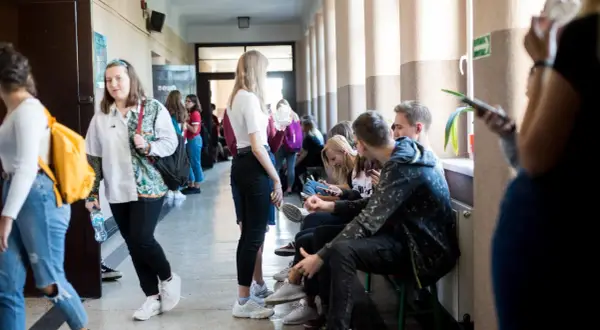 Uczniowie w szkolnym korytarzu, niektórzy siedzą, inni idą. Czy to sigma?