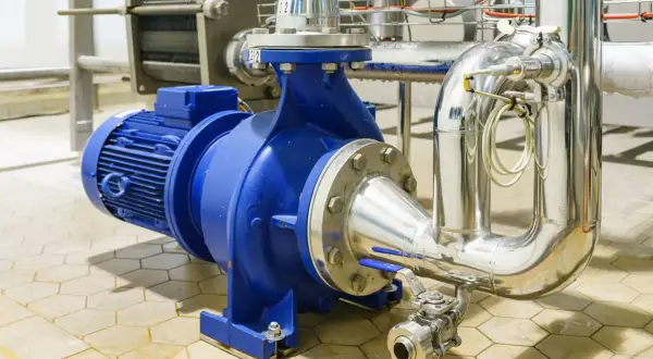 Pompe industrielle bleue connectée à des tuyaux en acier inoxydable. L'ensemble est conçu pour gérer des fluides sous haute pression.