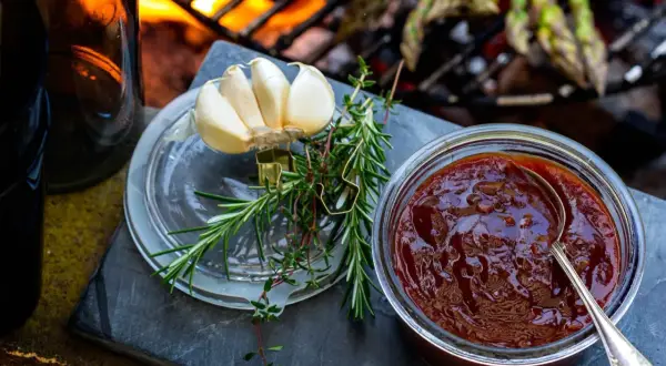 En burk med hemlagad bbq sås, vitlök och färska örter förbereds för grillen där sparris redan ligger på gallret.