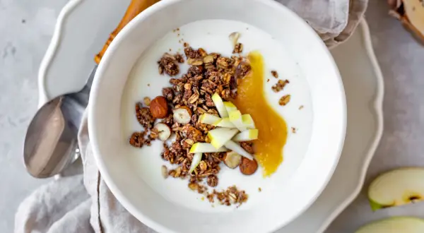 Schüssel mit Joghurt, knusprigem Granola, Nüssen, Apfelmus und Apfelstücken. Ein leckeres Frühstück!