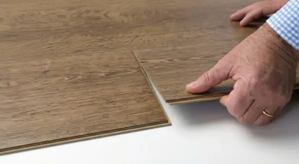 Close-up of a hand performing vinyl floor installation, clicking two wood-look planks together.