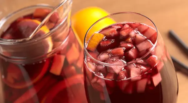Un bicchiere e una caraffa pieni di vino per sangria, con pezzi di frutta e fette d'arancia.