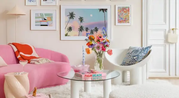 Ein Wohnzimmer im **danish pastel** Stil mit einem pinken Sofa, bunten Bildern und einer Vase voller Blumen.