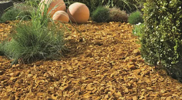 Ein schön angelegtes Beet mit Rindenmulch, Ziergräsern und dekorativen Kugeln.