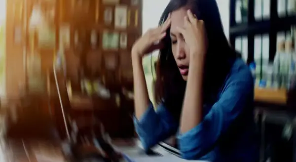 A woman with her hands on her head, looking distressed at a desk.