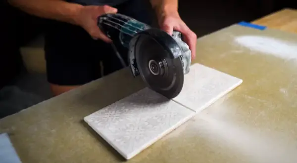 Hands carefully cutting decorative porcelain tile with an angle grinder, creating a clean line.