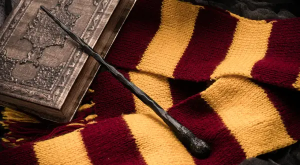 Magiczna różdżka i szalik w barwach Gryffindoru leżą obok ozdobnej księgi, idealne dla fanów szukających książek podobnych do Harrego Pottera.