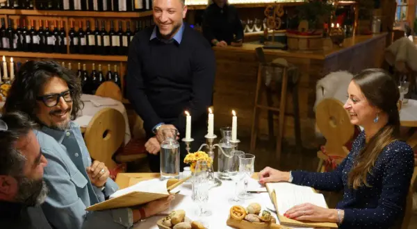 Un gruppo di amici ride a tavola in un ristorante di Milano, tra candele e bottiglie di vino.